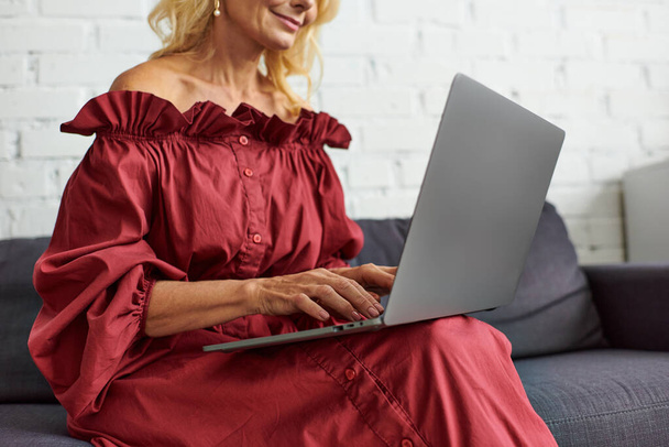 Stílusos nő elegáns öltözékben ül egy kanapén, lefoglal egy laptop használata. - Fotó, kép