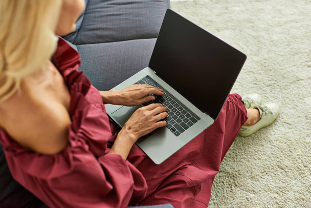 Una mujer con estilo absorto en su ordenador portátil mientras está sentado en un sofá en casa. - Foto, imagen