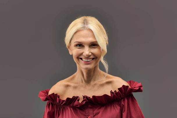 Une femme mature et élégante aux cheveux blonds dans un chemisier rouge, respirant la confiance et le style. - Photo, image