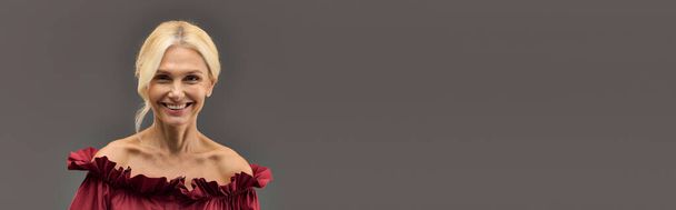 Una donna matura ed elegante in un abito rosso chic trasuda fiducia e luminosità, sorridendo con grazia. - Foto, immagini