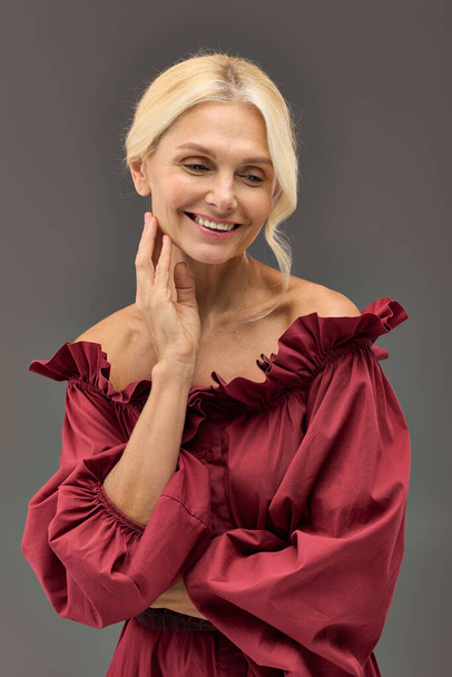 Μια ώριμη κομψή γυναίκα σε ένα κόκκινο κομψό φόρεμα χτυπά μια στάση. - Φωτογραφία, εικόνα