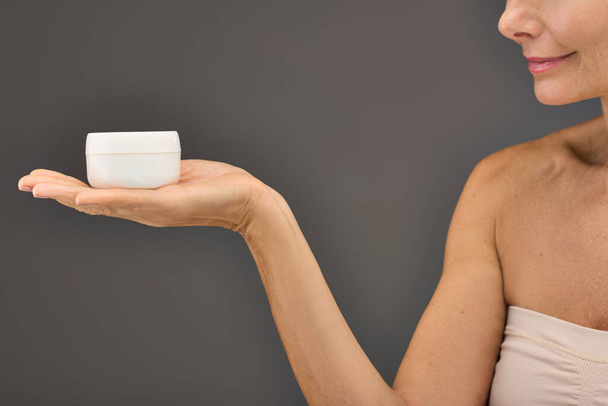 Donna matura elegantemente in possesso di una tazza di crema per la cura della pelle di routine. - Foto, immagini
