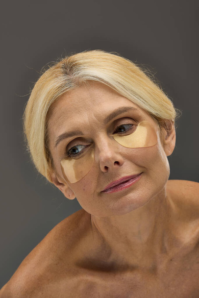 Attractive mature woman with blonde hair with eye patches on a gray backdrop. - Photo, Image