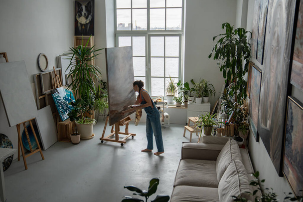 Naistaiteilija piirtää valotaiteen työpajassa. Nainen moderni nykyaikainen taidemaalari työskentelee maalaus tilava koti studio huone, varustettu luova työtila, koristeltu ruukkukasvit kukkia. - Valokuva, kuva
