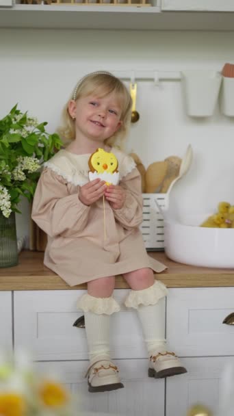 Szőke kislány világos ruhában mosolyog, miközben cukorkát tart csirke alakban.. - Felvétel, videó