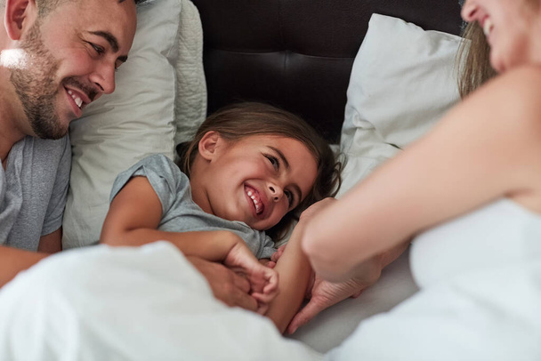Love, laughter and happy family in bed for tickle fun, playing or bonding at home together. Support, security and girl with funny parents in bedroom for wake up games with safety, care or protection. - Photo, Image