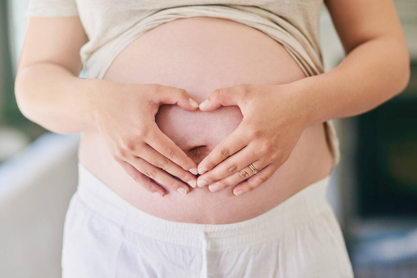 Χέρια, γυναίκα και έγκυο στομάχι με καρδιά για αγάπη ή ενθουσιασμό για την πατρότητα, μητρότητα και την αναμονή για την άφιξη του μωρού. Μητέρα να είναι, το σπίτι και την κοιλιά να αισθάνονται λάκτισμα για την άδεια μητρότητας - Φωτογραφία, εικόνα