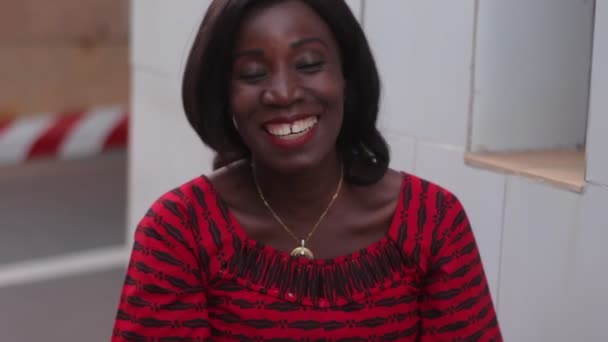 gyönyörű afrikai nő ül a szabadban a hagyományos ruha beszél, és nézi a kamera nevetés. - Felvétel, videó