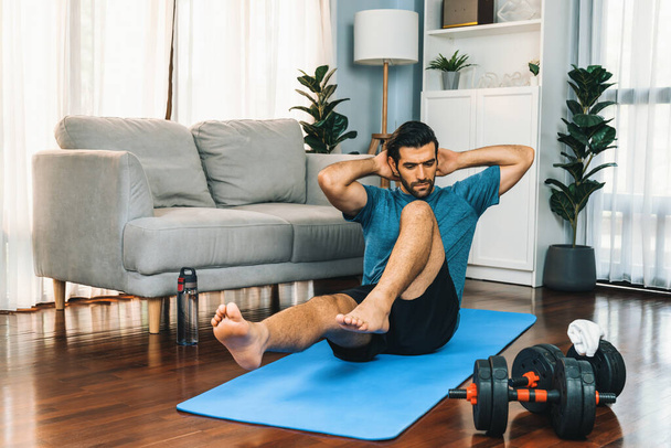 Athletic and sporty man doing crunch on fitness mat during home body workout exercise session for fit physique and healthy sport lifestyle at home. Gaiety home exercise workout training concept. - Photo, Image