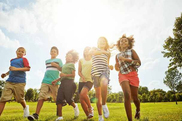 Boldog gyerekek, nyár és futás barátokkal a természetben a szórakozás, játékos nap vagy napsütés a parkban. Sokszínűség vagy csoport izgatott gyermekek vagy fiatalok élvezik napos szabadtéri nyaralás fűpályán együtt. - Fotó, kép