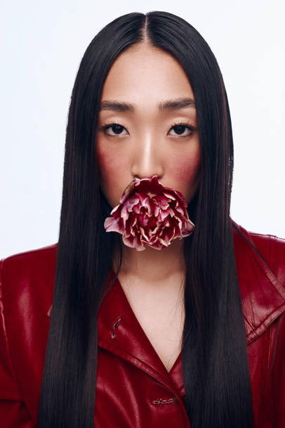 Hermosa mujer con el pelo largo y negro usando una chaqueta roja y sosteniendo una flor en su boca - Foto, Imagen