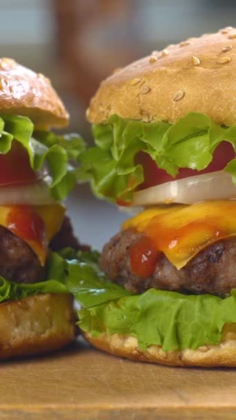 Große appetitliche Burger mit frischen Tomaten, Zwiebeln, saftigen gegrillten Rindfleischpatty und Käse. Fast Food, Nahaufnahme, vertikales Filmmaterial - Filmmaterial, Video