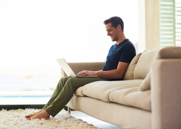 Sofa, smile and man with typing on laptop at home for communication, connection and freelance website. Relax, remote work and male person with technology for digital article, research and information. - Photo, Image