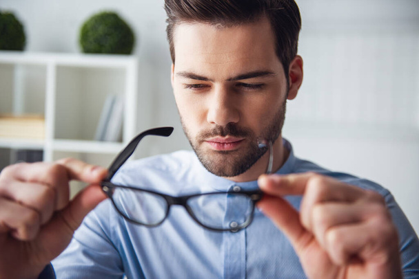 Красивий стомлений бізнесмен дивиться на свої окуляри і думає під час роботи в офісі
 - Фото, зображення