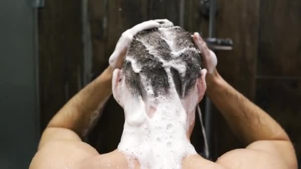 Sexy seductive Caucasian man in shower washing head showering in bathroom at home close up. Тысячелетний брюнетка парень ополаскивая шампунь и кондиционер от волос в теплой ванне горячая вода течет вниз  - Кадры, видео