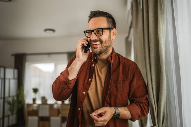 Ritratto di uomo adulto in piedi mentre parlare sul cellulare e sorridere a casa felice, rilassarsi - Foto, immagini