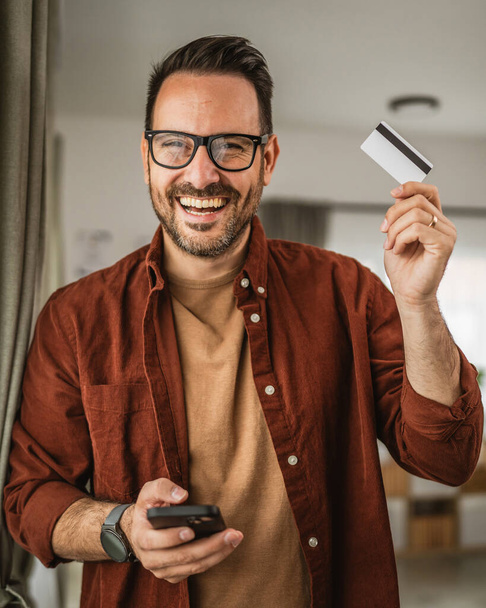 Ritratto di uomo adulto negozio online con cellulare e tenere la carta di credito a casa - Foto, immagini
