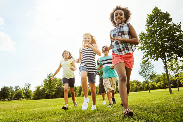 Szczęśliwi przyjaciele, różnorodność i bieganie z dziećmi w przyrodzie dla zabawy, zabawy dzień lub lato w parku. Grupa podekscytowanych dzieci lub młodzieży korzystających słoneczne wakacje na świeżym powietrzu lub weekend na trawie razem. - Zdjęcie, obraz