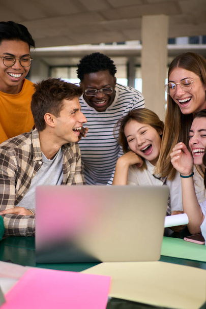 大学キャンパスのカフェテリアでラップトップを使用して笑う若い多様な学生の垂直グループ. クリエイティブカレッジプロジェクトに取り組む多民族クラスメイトと一緒に勉強 - 写真・画像