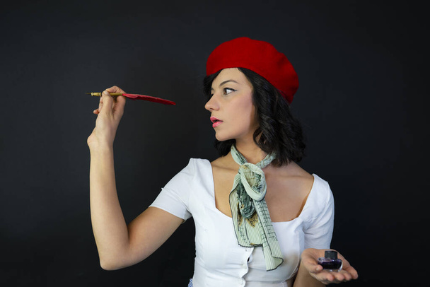 Женщина в красной шляпе и белой рубашке держит ручку и бутылку чернильницы для рекламы - Фото, изображение