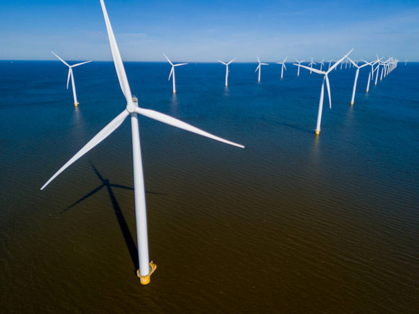 Un grupo de majestuosas turbinas eólicas de pie en el océano contra un cielo nublado, aprovechando el poder del viento para generar energía sostenible. vista aérea de aviones no tripulados de turbinas de molino de viento  - Foto, Imagen
