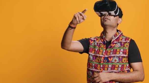 Indiase man draagt virtual reality headset, doet vegen gebaren. Technologie liefhebber met behulp van high tech futuristische moderne VR gadget, geïsoleerd over studio achtergrond, camera A - Video