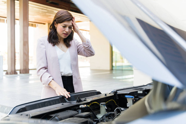 Besorgte junge Frau in Businesskleidung untersucht ihren Automotor und ist frustriert über plötzliche Fahrzeugpanne auf Parkplatz - Foto, Bild