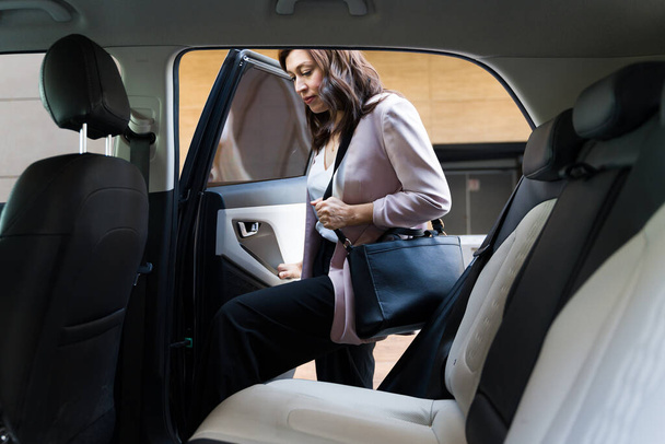 Профессиональная деловая женщина заходит в автомобиль, изображая ежедневный транспорт в корпоративном городском стиле жизни - Фото, изображение