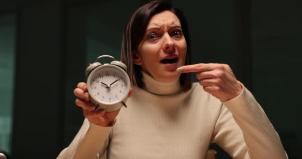 La señora exhausta señala que el reloj despertador vintage se queda hasta tarde en el trabajo. Cansancio femenino palpable como testimonio de un compromiso inquebrantable con los deberes - Metraje, vídeo