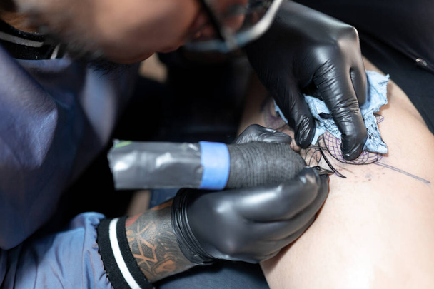 A tattoo artist is tattooing a snake on a woman's leg. Close up. Concept of tattoo studio - Photo, Image