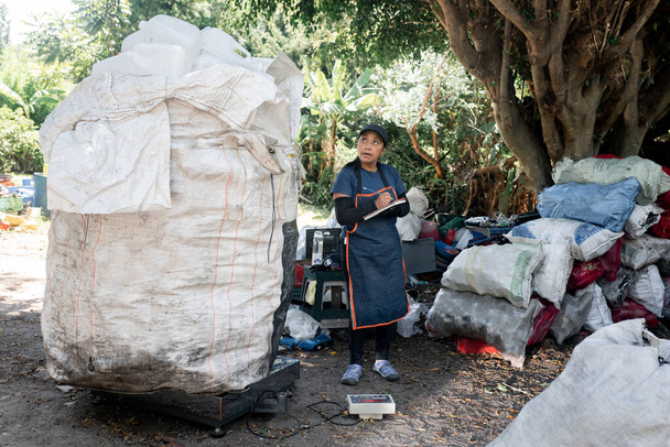 Латиноамериканка управляет переработанным пластиком на месте переработки, отмечая вес для эффективного управления отходами - Фото, изображение