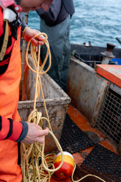 ロブスター漁船のロープで働く若い男性漁師の垂直クローズアップ - 写真・画像