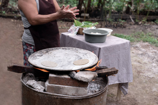 Dospělá hispánka ručně formuje kukuřičné tortilly a vaří je nad kamny v přírodě v Guatemale. Místní pojetí jídla - Fotografie, Obrázek