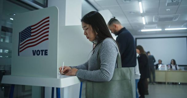 Asian woman comes to voting booths in polling station office. National Election Day in United States. Political races of US presidential candidates. Concept of civic duty and patriotism. Dolly shot. - Photo, Image