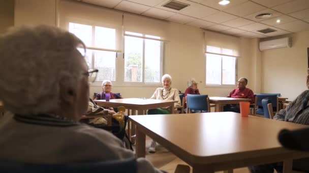 Μεγέθυνση σε αργή κίνηση των ηλικιωμένων που κάθονται στα τραπέζια στο φωτεινό δωμάτιο του γηροκομείου κατά τη διάρκεια της ημέρας - Πλάνα, βίντεο