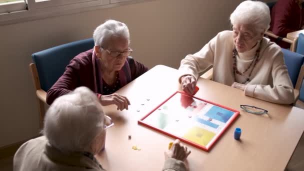 Dall'alto degli amici anziani di sesso maschile e femminile che trascorrono il tempo libero mentre giocano al ludo a tavola nella mensa della casa di cura - Filmati, video