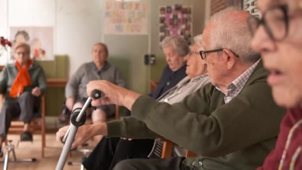 Starsi mężczyźni i kobiety ćwiczą siedząc na krzesłach podczas sesji fizjoterapii w ośrodku rehabilitacyjnym - Materiał filmowy, wideo