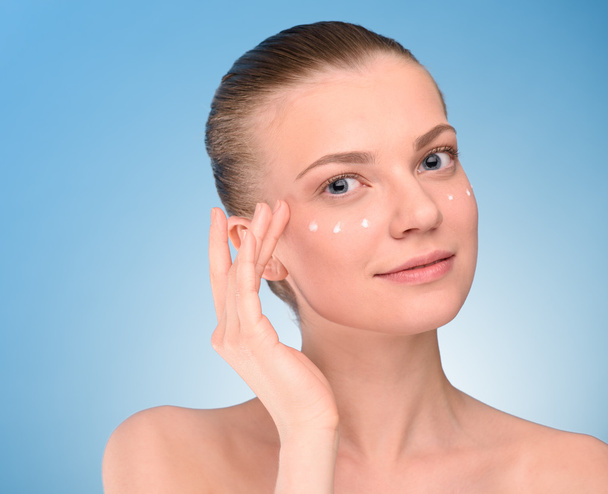 Woman applying lifting cream on face, over blue background. - Fotó, kép