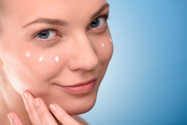 Woman applying lifting cream on face, over blue background. - Fotoğraf, Görsel