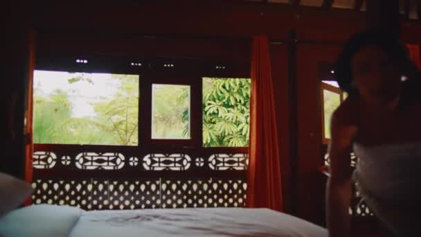 Vista interna offuscata, camera da letto accogliente con morbide lenzuola e uno scorcio di verde attraverso la finestra, che trasmette un'atmosfera tranquilla durante la mattina - Filmati, video