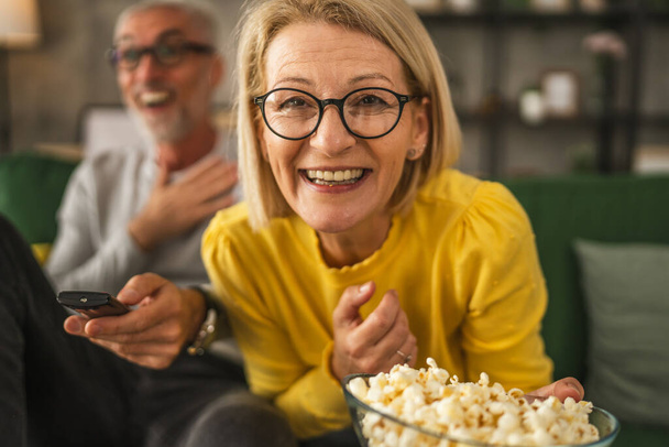 zbliżenie w górę w Dojrzałe seniora kobieta głowa uśmiech i oglądać film i trzymać popcorn z mężczyzna mąż w tle - Zdjęcie, obraz