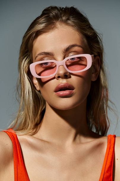 Uma mulher elegante em óculos de sol rosa e um top laranja exala uma vibração de verão divertida e colorida. - Foto, Imagem