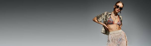 Mulher loira faz uma pose graciosa em um biquíni elegante contra um simples pano de fundo cinza. - Foto, Imagem