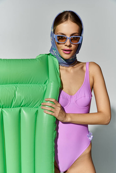 Fashionable blonde woman in purple swimsuit holding inflatable mattress. - Photo, Image