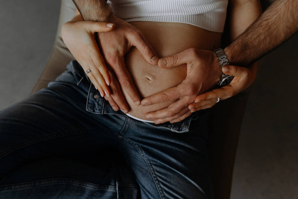 Ein Paar formt mit den Händen ein Herz auf dem Schwangerschaftsbauch. Konzept der Schwangerschaft, der Geburt eines Kindes, Pflege. - Foto, Bild