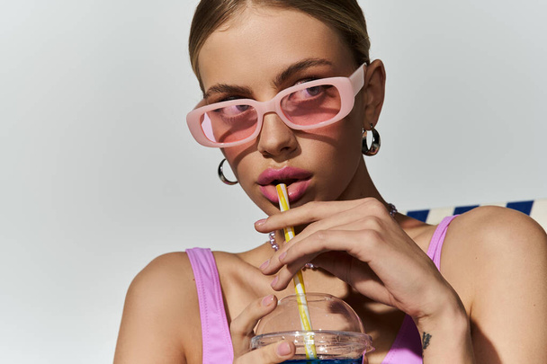 Ξανθιά γυναίκα με ροζ γυαλιά ηλίου πίνοντας μέσα από ένα καλαμάκι. - Φωτογραφία, εικόνα
