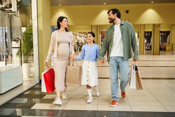 Wesoła rodzina, naładowana torbami na zakupy, spaceruje po tętniącym życiem centrum handlowym w zabawny weekend zakupowy. - Zdjęcie, obraz