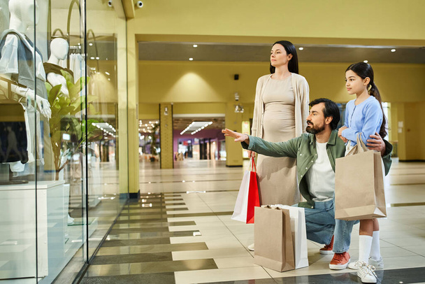 Una famiglia felice esamina le loro borse della spesa in un centro commerciale occupato durante una divertente gita di fine settimana. - Foto, immagini