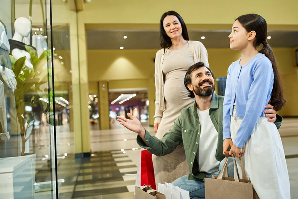 Μια χαρούμενη οικογένεια περπατά σε ένα εμπορικό κέντρο με πολύχρωμες τσάντες για ψώνια. - Φωτογραφία, εικόνα