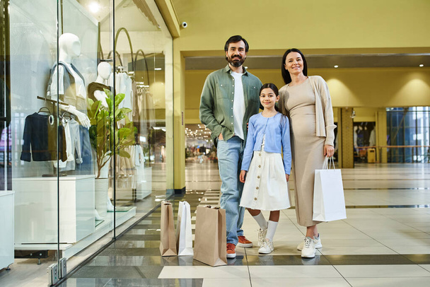 Μια χαρούμενη οικογένεια, φορτωμένη με τσάντες για ψώνια, απολαμβάνοντας μια χαλαρή ημέρα της θεραπείας λιανικής σε ένα πολυσύχναστο εμπορικό κέντρο. - Φωτογραφία, εικόνα